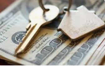 Earnest money shown with house key and home shaped keychain on top of hundred dollar bills