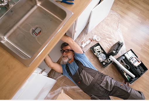 Handyman repairing plumbing under a kitchen sink, preparing the home for sale with essential pre listing repairs.